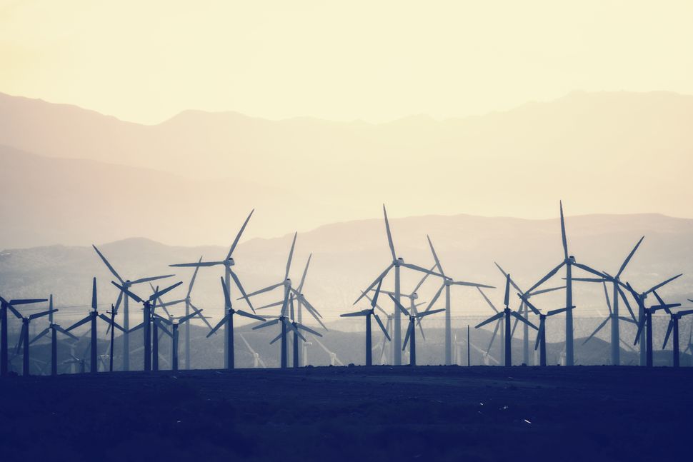 The sun begins setting over a field of wind turbines.